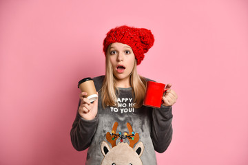 Teenage female in gray reindeer pajamas, red hat. She holding ceramic and paper cups, smiling,...