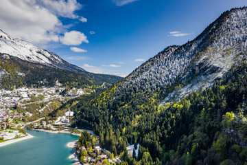 The Improbable aerial landscape of village Molveno, Italy, azure water of lake, empty beach, snow covered mountains Dolomites on background, roof top of chalet, sunny weather, a piers, coastline, 