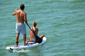 Attractive young couple riding tandem on a paddle board.