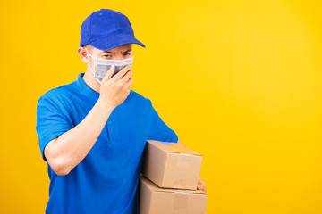 Fototapeta na wymiar Asian young delivery worker man in blue t-shirt and cap uniform wearing face mask protective he sneezing during service customer under coronavirus or COVID-19, studio shot isolated yellow background