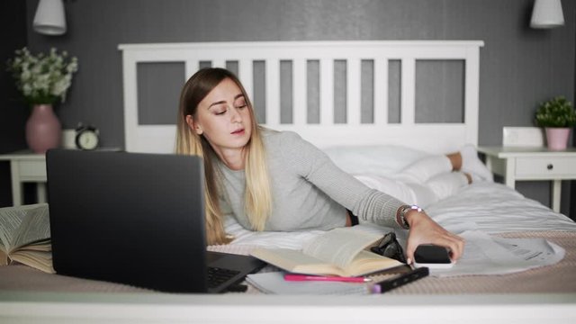 Young woman lying on the bed typing on notebook and using smartphone