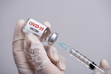 Female doctor hand wearing white grove and holding syringe and COVID-19 vaccine. Healthcare and...