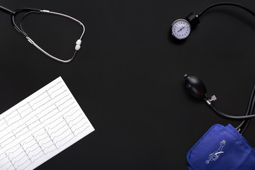 Device for measuring blood pressure. Tonometer, cuff, stethoscope, cardiogram on a black background. Copy space for inserting text. View top.