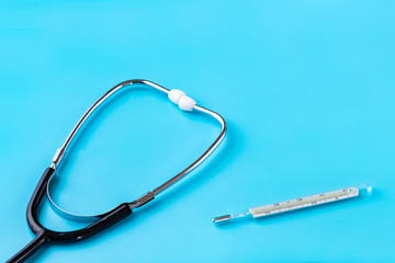 Stethoscope and glass thermometer for measuring body temperature on a blue background. Copy space....