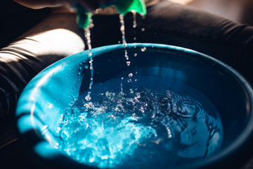 The woman squeezes a cloth over the blue bucket © Dragica