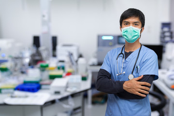 portrait of a Asian young man nurse/Doctor/scientist wearing surgical mask and standing with his arms crossed, Laboratory background