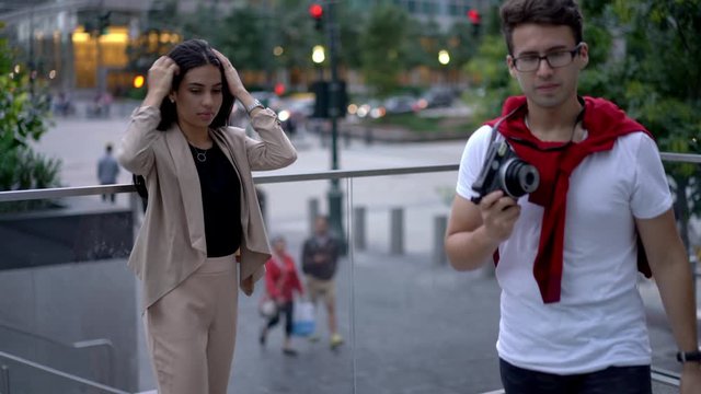 Latino American hipster girl dressed in trendy apparel preparing for posing on urban setting asking Spanish boyfriend for taking some pictures on old fashioned camera
