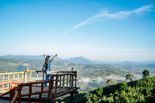 Beautiful asian tourist traveler girl on holiday adventure traveling on the mountains, walking along the path smiling in the morning sunrise and misty mountains view wearing a denon jacket and jeans