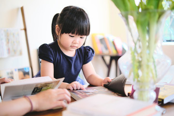 Cute asian girl learning by reading and studying books and playing at home in the living room sitting, home schooling education for children, feeling happy cheerful, and enjoying staying at home