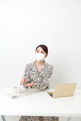 マスクをしながらリモートワーク中に手の消毒をしている女性