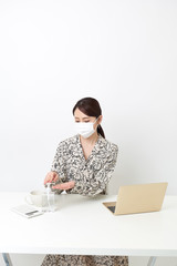 マスクをしながらリモートワーク中に手の消毒をしている女性
