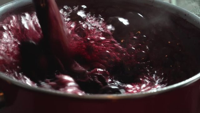 Cooking delicious red fruit jam, mixing and kneading. Close up. Jabuticaba or jaboticaba jam. Cook jaboticaba, which boils and foam in a ceramic lined pan.