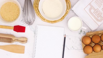 Cooking supplies and notebook for recipe appear on marble table - Stop motion 