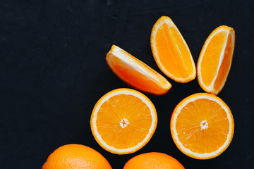 Halves and slices of fresh juicy oranges on black textured background.