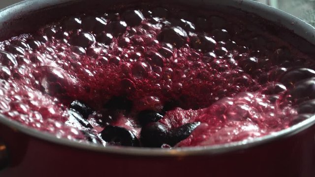 Cooking delicious red fruit jam, mixing and kneading. Close up. Jabuticaba or jaboticaba jam. Cook jaboticaba, which boils and foam in a ceramic lined pan.