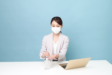 マスクをしてリモートワークしながら手を消毒している女性