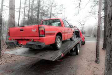 Fototapeta na wymiar Red pickup truck being loaded on red tilt bed tow truck to be hauled away