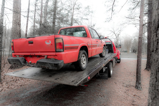 Red pickup truck being loaded on red tilt bed tow truck to be hauled away