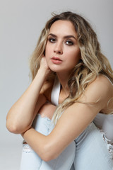 Young pretty in jeans and shirt woman sitting on gray background