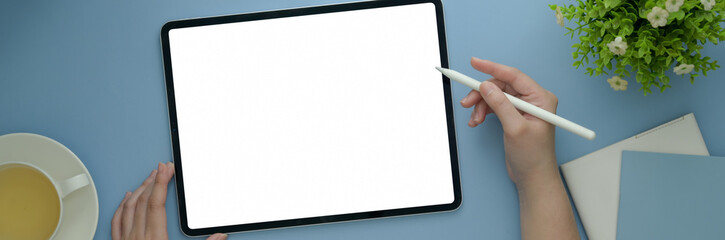 Obraz premium Overhead shot of female freelancer working on blank screen tablet on light blue table