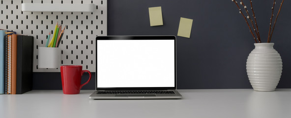 Close up view of stylish office desk with blank screen laptop, mug, office supplies, decorations and copy space