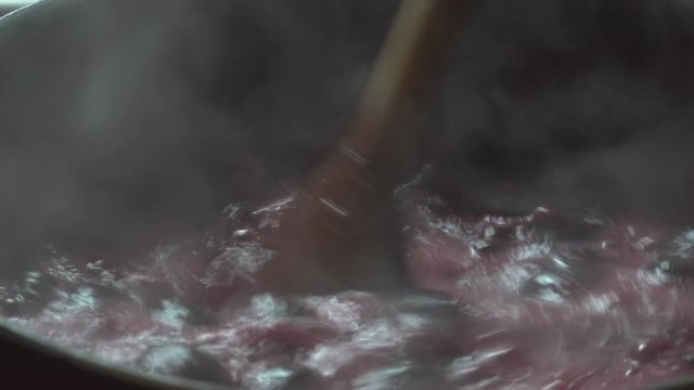 Cooking delicious red fruit jam, mixing and kneading. Close up. Jabuticaba or jaboticaba jam. Cook jaboticaba, which boils and foam in a ceramic lined pan.