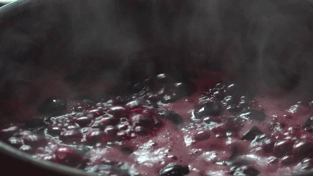 Cooking delicious red fruit jam, mixing and kneading. Close up. Jabuticaba or jaboticaba jam. Cook jaboticaba, which boils and foam in a ceramic lined pan.