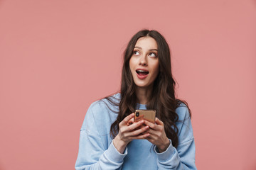 Image of astonished young woman looking aside and using cellphone