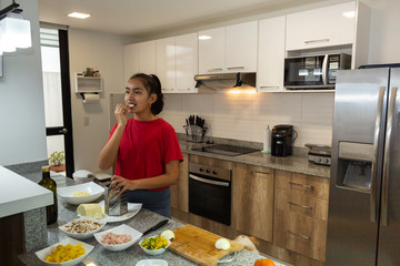 Teen girl testing a piece of cheese while preparing pizza at home