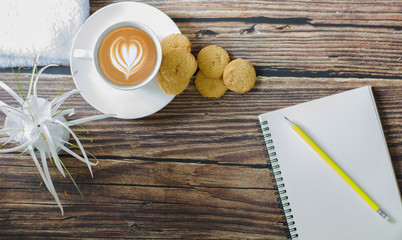 Top view a cup of hot coffee with .butter cookies,  notebook and flower on a wooden table holiday home vacation ideas