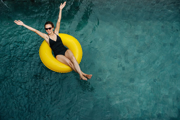 Young woman reaching for the sky in pool happily swimming on an inflatable buoy.