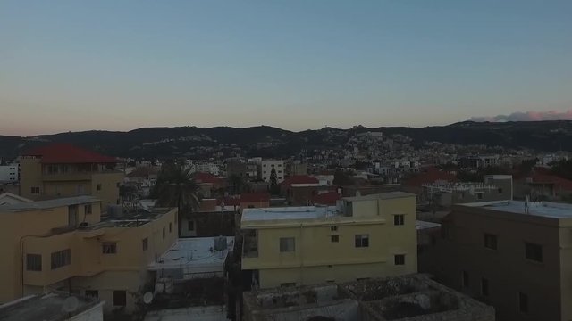 Low aerial rising drone shot above buildings reveal Batroun village at sundown, Lebanon