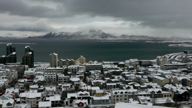Aerial long shot cityscape of snowy Reykjavik with Mount Esja at the background during winter