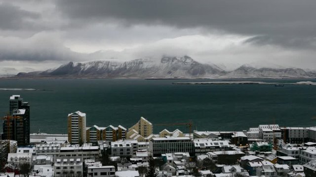 Aerial long shot cityscape of snowy Reykjavik with Mount Esja at the background during winter