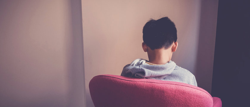 Sad preteen boy sitting alone in chair facing wall, depressed,introvert,  autism awareness, children mental health,psychology teen autism spectrum disorder, social distancing, self isolation concept