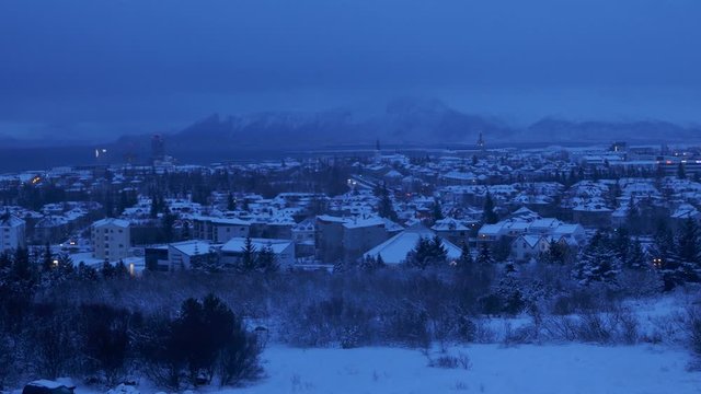 Aerial long shot cityscape night shot of snowy Reykjavik with Mount Esja at the background during winter
