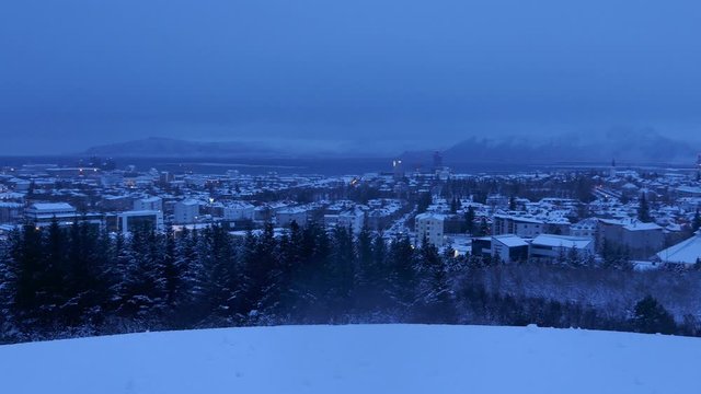 Aerial long shot cityscape night shot of snowy Reykjavik with Mount Esja at the background during winter
