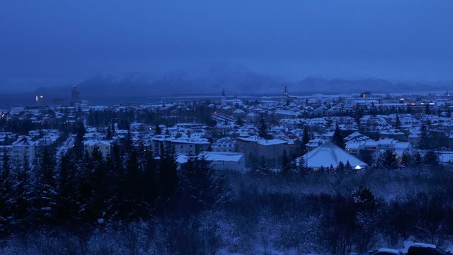 Aerial long shot cityscape night shot of snowy Reykjavik with Mount Esja at the background during winter