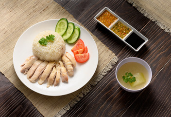 Hainanese chicken rice with soup and three sauces on dark wood table texture