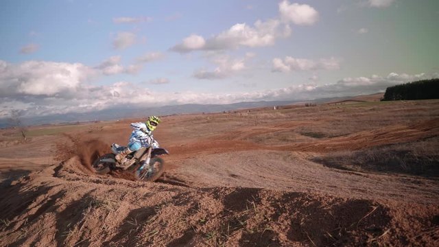 A guy riding a motorcycle on a motocross track, splashing dirt as he goes by.