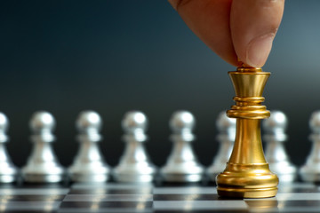 Businss man hand hold gold king chess piece to movement when face with silver team on black background (Concept for company strategy, business decision and encounter the problem)