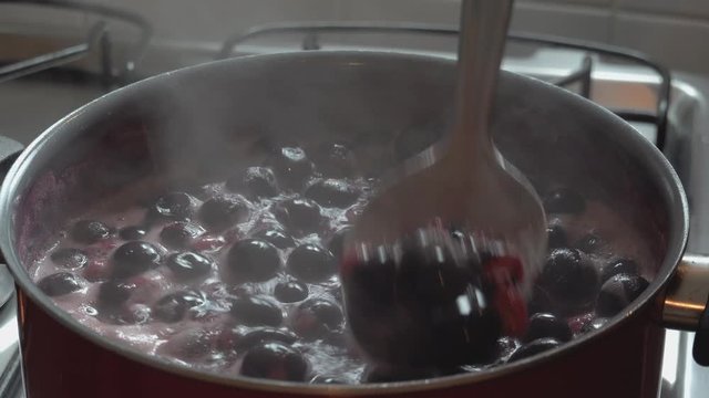 Cooking delicious red fruit jam, mixing and kneading. Close up. Jabuticaba or jaboticaba jam. Cook jaboticaba, which boils and foam in a ceramic lined pan.