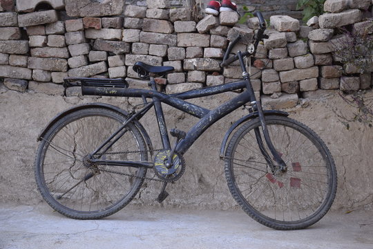 Old black colored bicycle of children resting on the wall, concept of Indian village