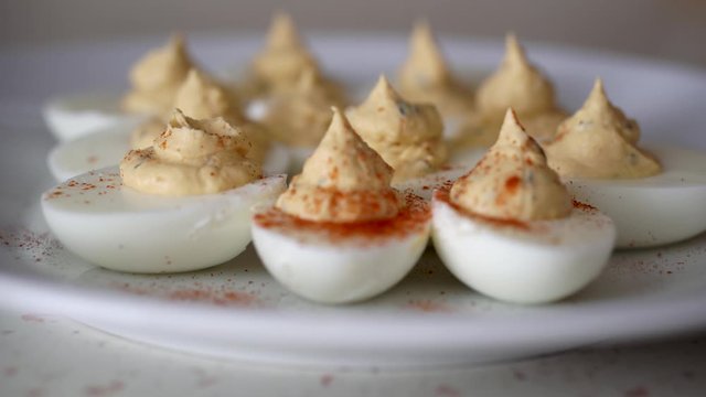 Sprinkling deviled eggs on white plate with bright red dried paprika.