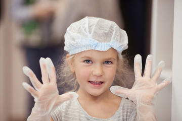 Portrait of a happy girl in a disposable uniform, wearing gloves and a hat, a cooking class