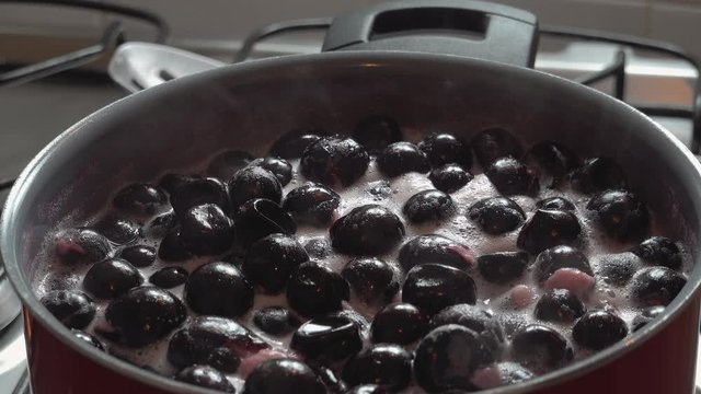 Cooking delicious red fruit jam, mixing and kneading. Close up. Jabuticaba or jaboticaba jam. Cook jaboticaba, which boils and foam in a ceramic lined pan.