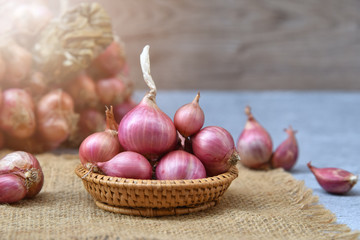 Thai red onion or Shallots. Fresh purple shallots on bamboo basket with old wallpaper and shallots bunch background. Selected focus. Concept of spices in healthy cooking