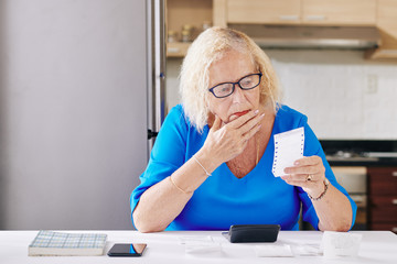 Pensive senior woman rubbing her chin when checking bills