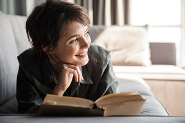 Image of caucasian cute pleased woman reading book and smiling