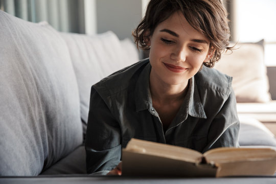 Image of brunette cute pleased woman reading book and smiling
